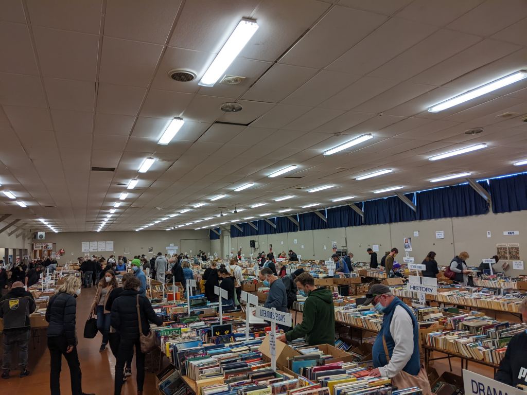 A large hall lined with trestle tables covered in books, and people browsing.