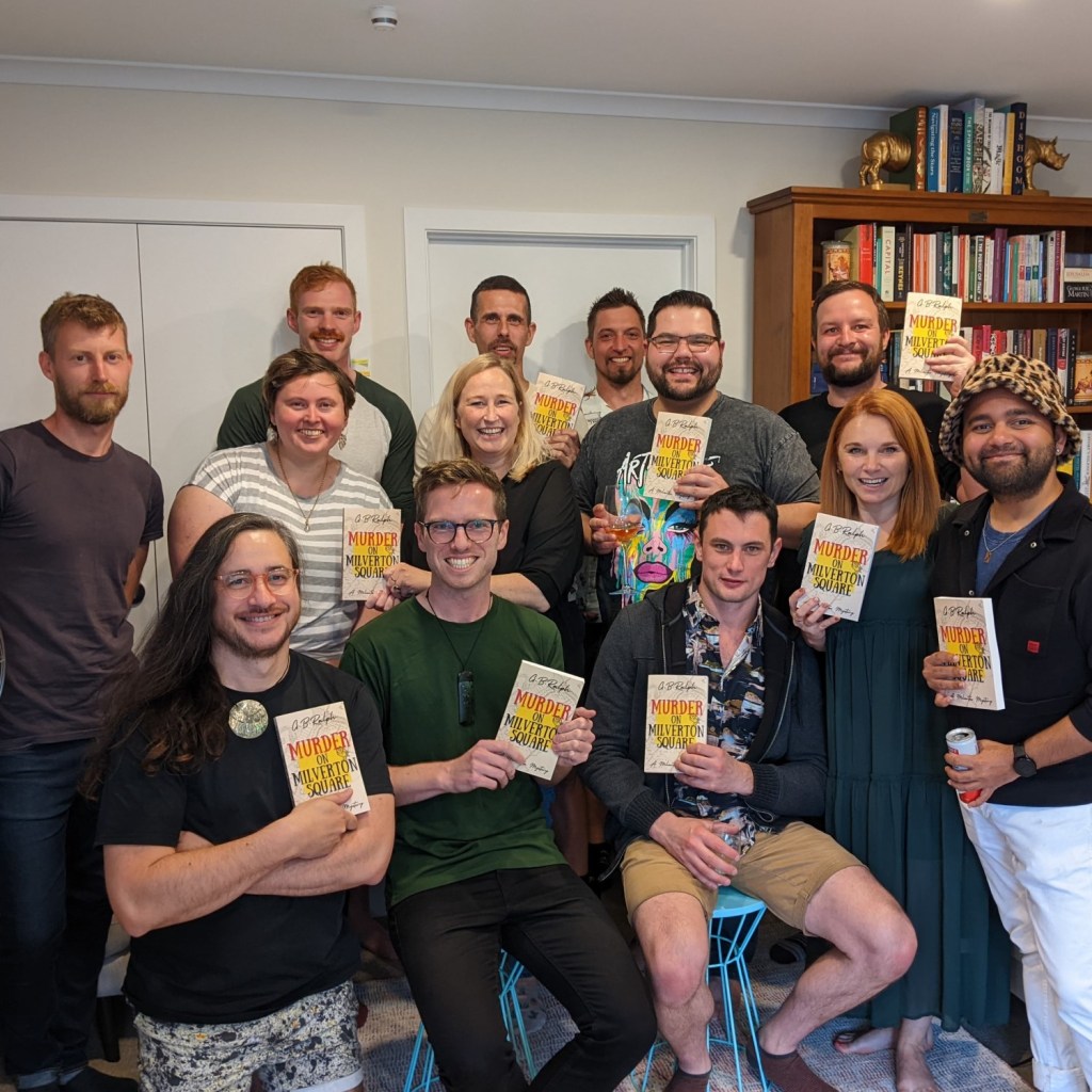 Group of friends holding paperback copies Murder on Milverton Square (A Milverton Mystery) by G B Ralph. 