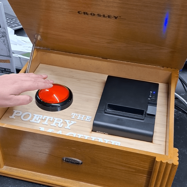 A hand hovering over a big red button on a contraption labelled "The Poetry Machine"