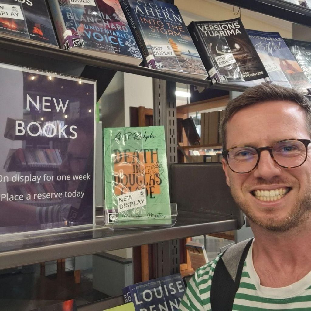 Author G B Ralph selfie with Death in Douglas Glade paperback on the New Books shelf at the library