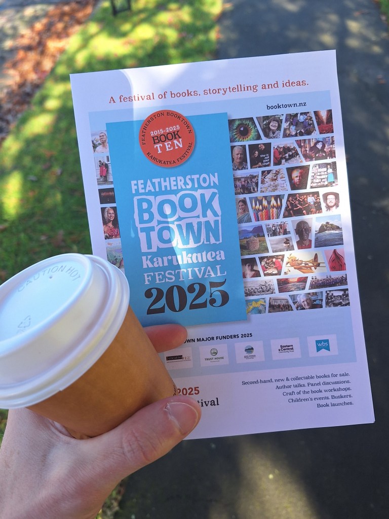 Featherston Booktown Karukatea Festival 2025 programme held in hand with a takeaway coffee.