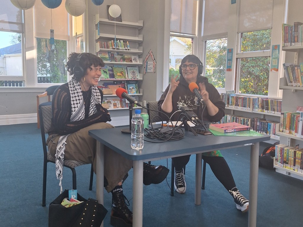 Two authors sitting at table with microphones and headsets, talking.
