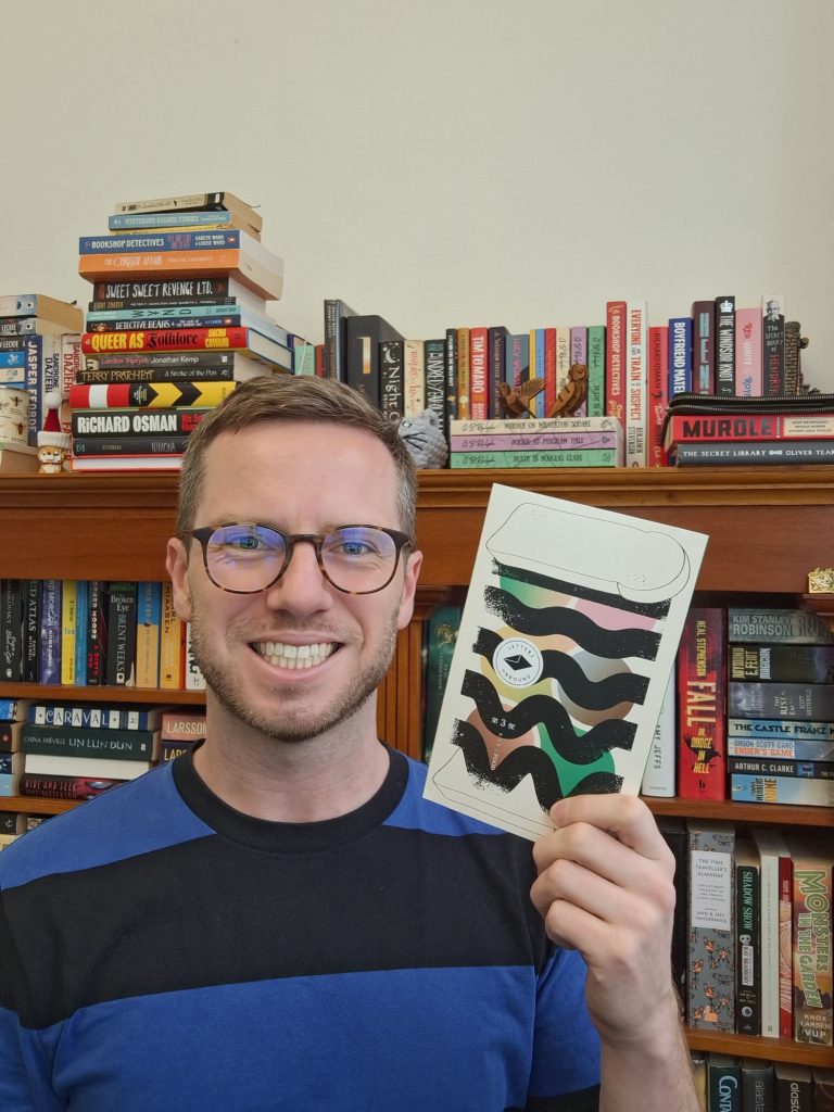 Author G. B. Ralph holding up a book in front of bookcases