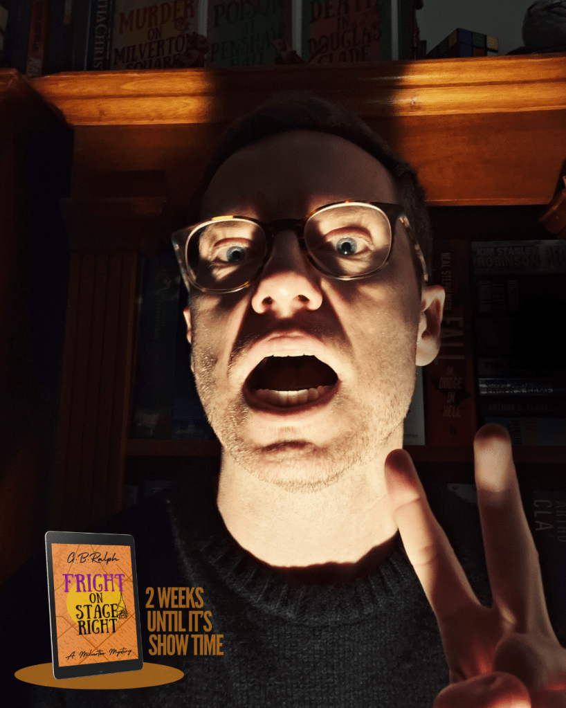 Selfie of a spookily underlit face and a hand with two fingers up. Fright on Stage Right (A Milverton Mystery) by G. B. Ralph. Book cover image and text reading: 2 weeks until it's show time. Bookshelves in shadow in the background.