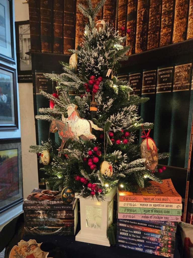 A stack of Milverton Mysteries paperback books under a small decorated Christmas tree