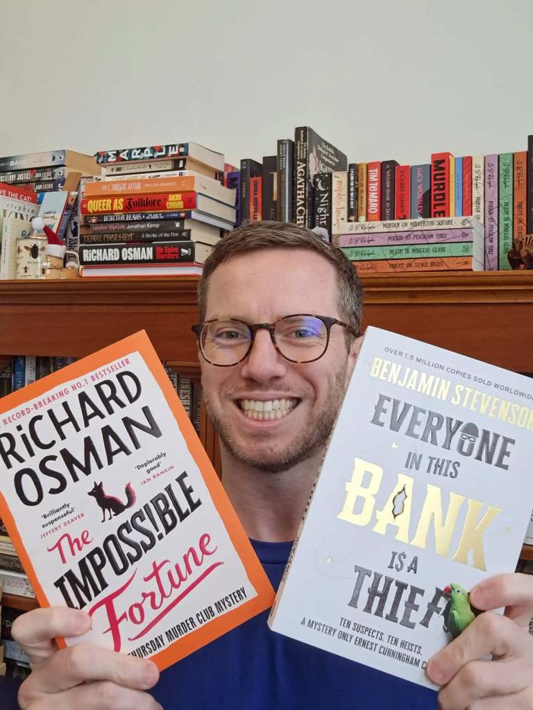 G. B. Ralph selfie holding up two paperback books: The Impossible Fortune by Richard Osman and Everyone in This Bank Is a Thief by Benjamin Stevenson.