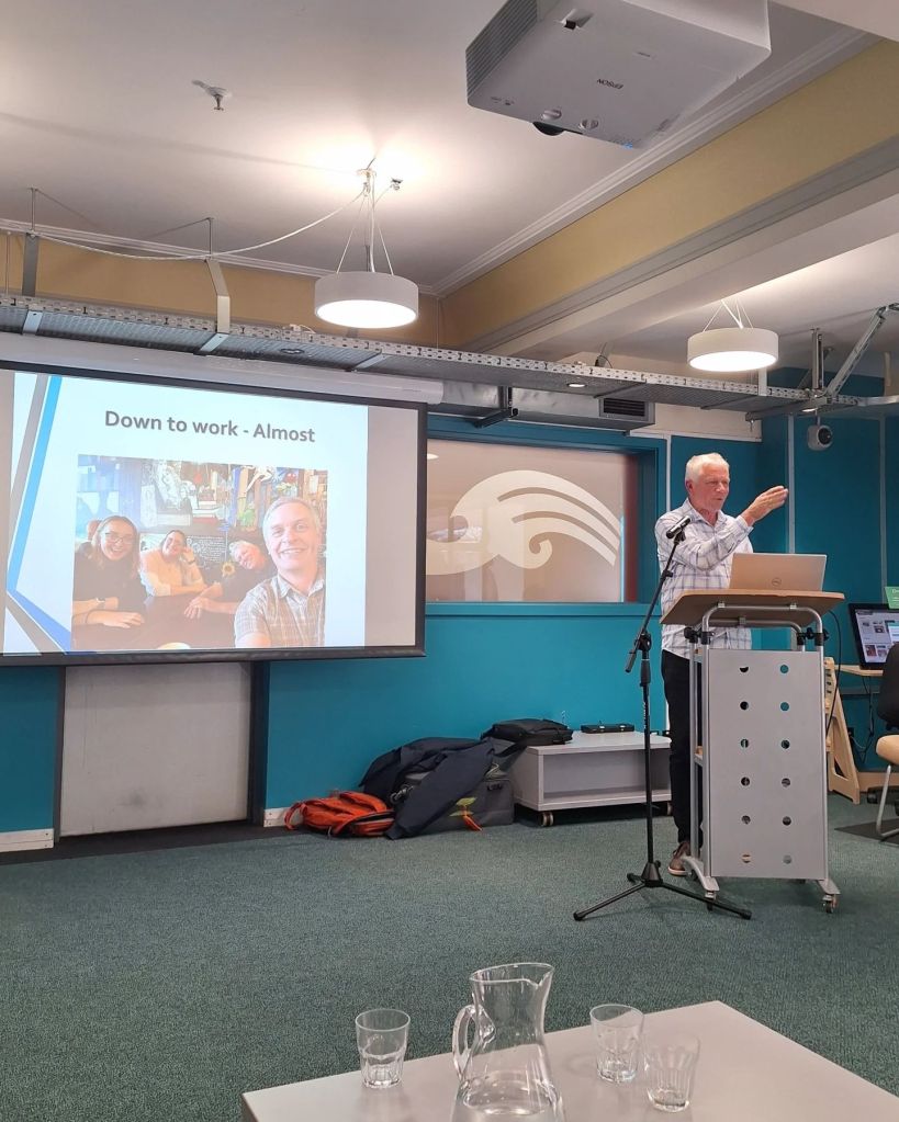 Riley Chance at a lectern speaking in front of a slideshow presentation
